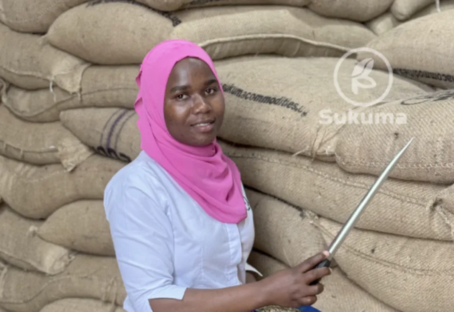 Sukuma team member beside a wall of stacked jute coffee sacks